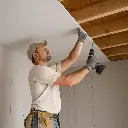 Drywall Installation – Contractor Securing Ceiling Panel with Drill.webp